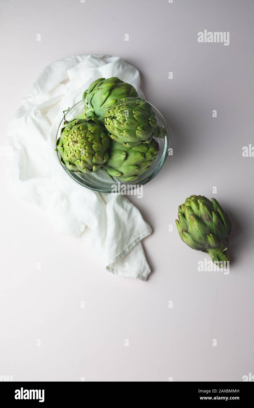 Carciofi in una ciotola di vetro e una drappiera bianca su uno sfondo bianco chiaro e arioso Foto Stock