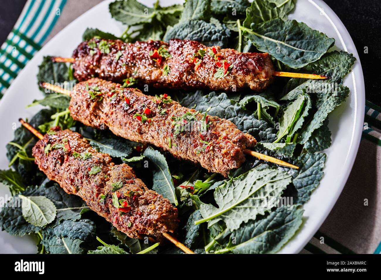 Agnello alla griglia kebab kofta su spiedini di legno su un letto di foglie di kale fresco servito su un piatto bianco con un tovagliolo, primo piano Foto Stock