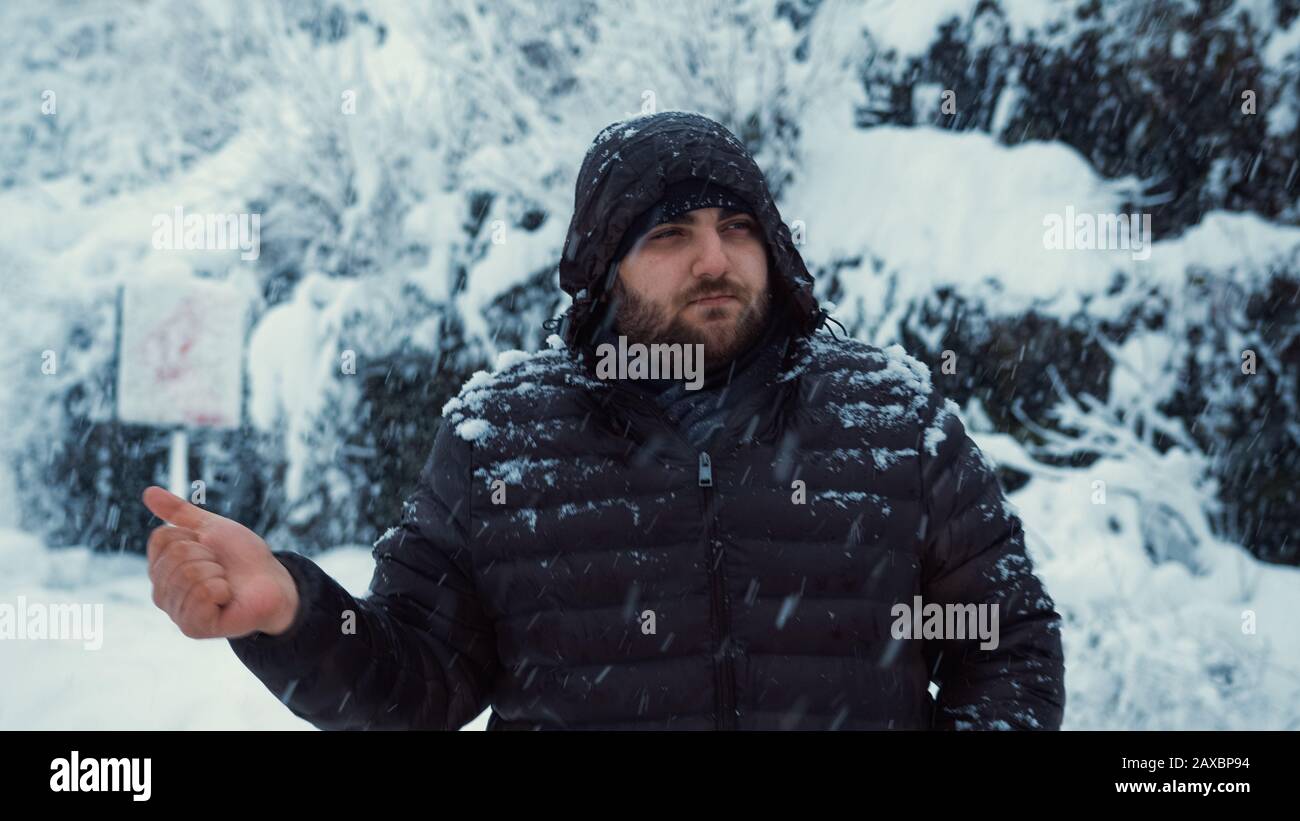 Mentre si nevica in una giornata invernale, l'uomo freddo è hitchhiking. Hitchhiking Concetto. Foto Stock