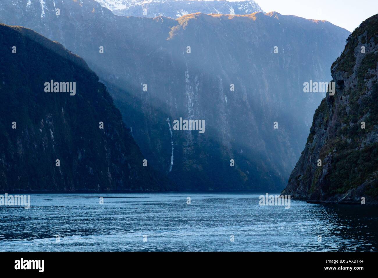 Il sole del mattino manda alberi di luce a Milford Sound, Nuova Zelanda Foto Stock