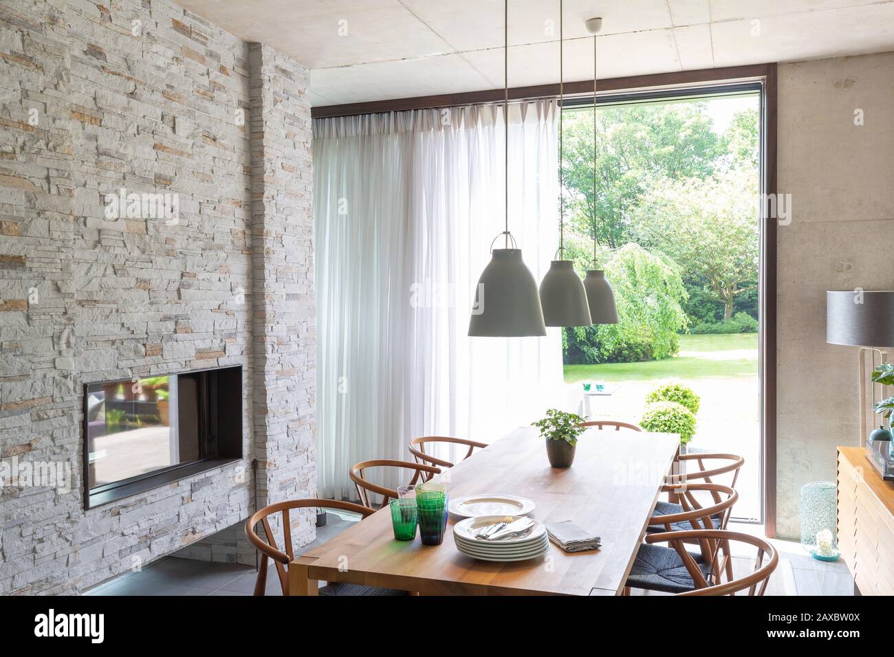 Lampada a sospensione sul tavolo da pranzo in una moderna sala da pranzo con camino in mattoni Foto Stock