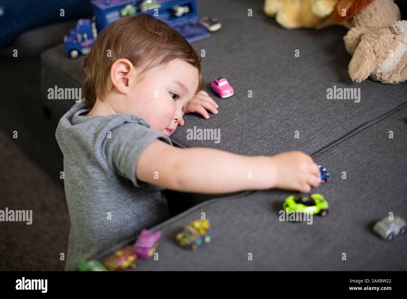 Curiosa ragazza carino toddler giocare con le auto giocattolo sul divano Foto Stock
