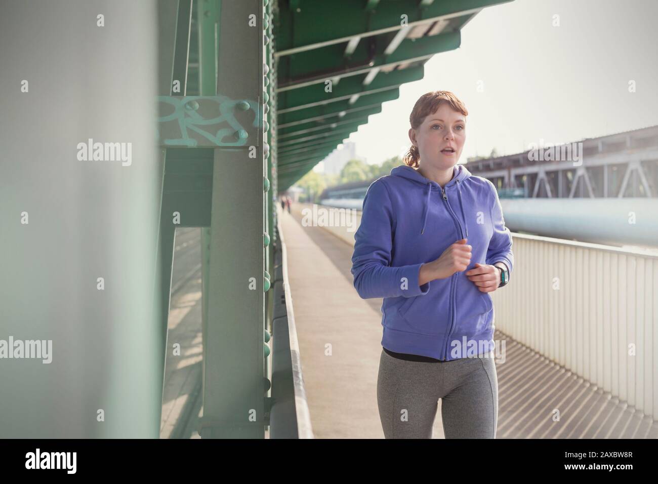 Giovane donna dedicata che corre lungo la piattaforma soleggiata stazione ferroviaria Foto Stock