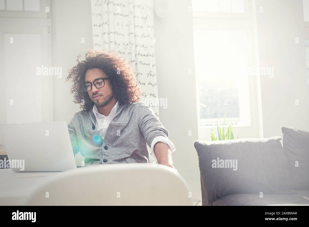 Giovane uomo che lavora su un computer portatile in un salotto soleggiato Foto Stock