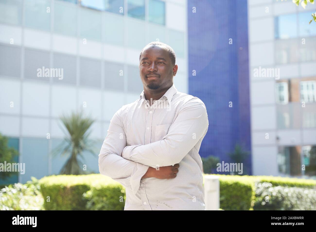 Ritratto giovane sicuro con braccia incrociate fuori soleggiato edificio Foto Stock