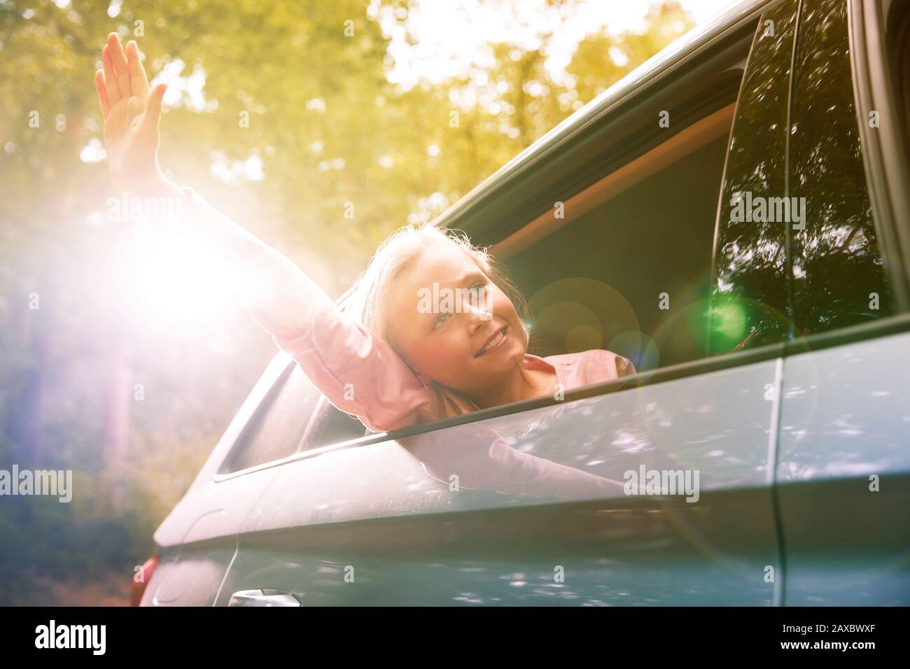 Ragazza spensierata che raggiunge il braccio fuori finestra soleggiata auto Foto Stock