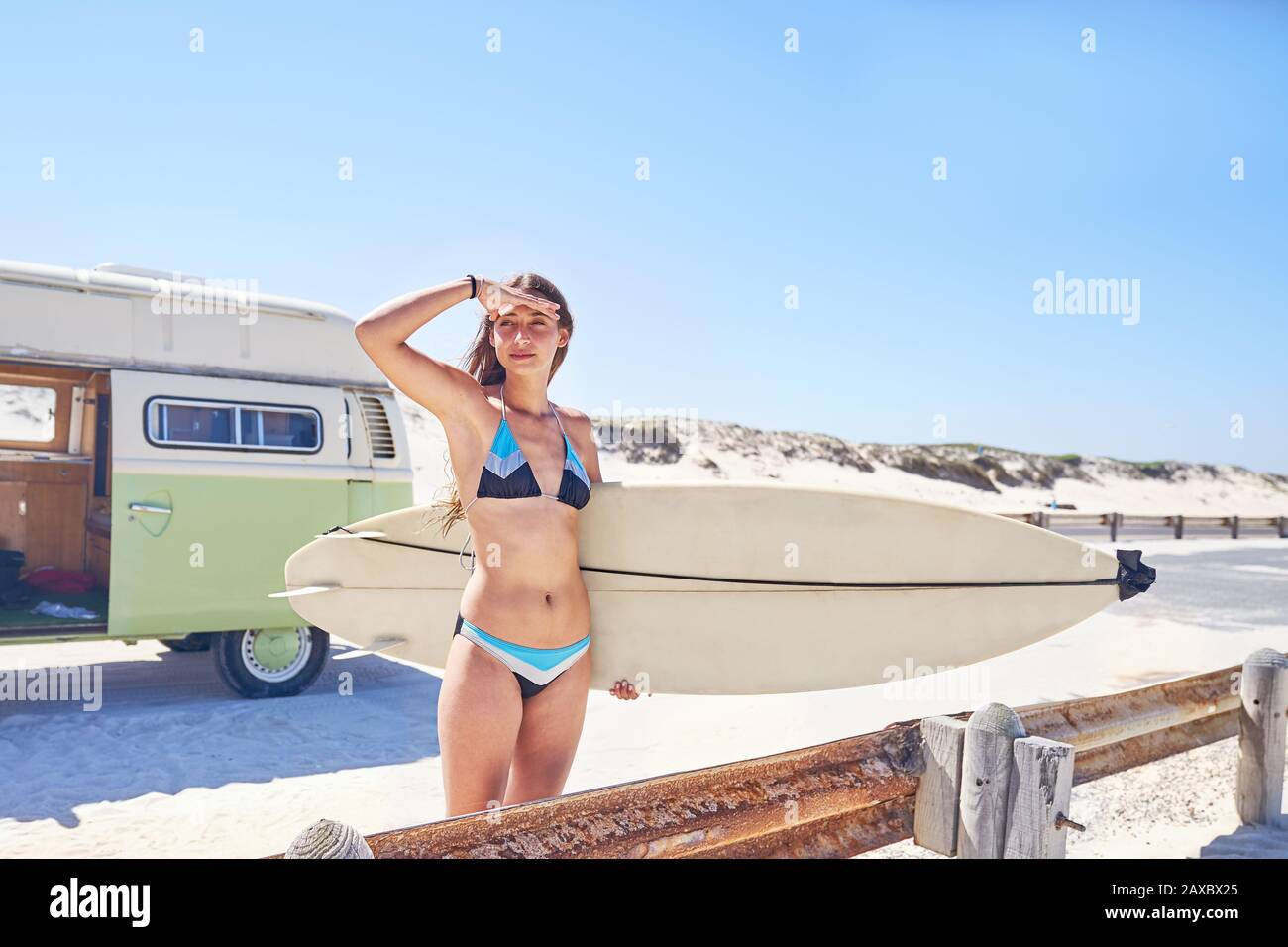 Giovane surfista femminile con tavola da surf sulla soleggiata spiaggia estiva Foto Stock