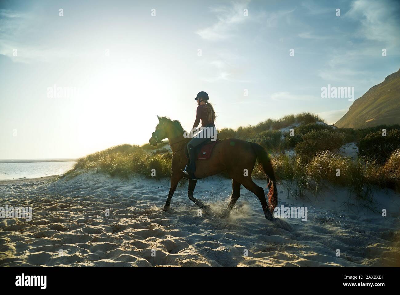 Giovane donna a cavallo sulla spiaggia soleggiata tranquilla Foto Stock