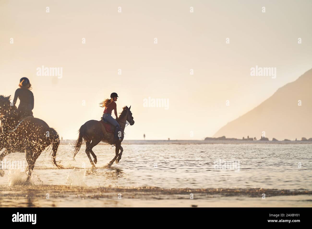 Giovani donne equitazione in mare surf al tramonto Foto Stock