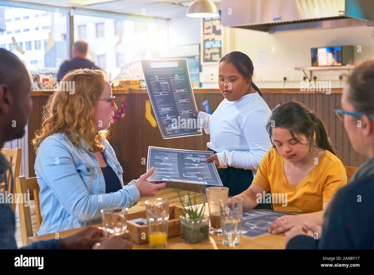 La sindrome Di Down del server femminile giovane che dà i menu ai clienti nel caffè Foto Stock