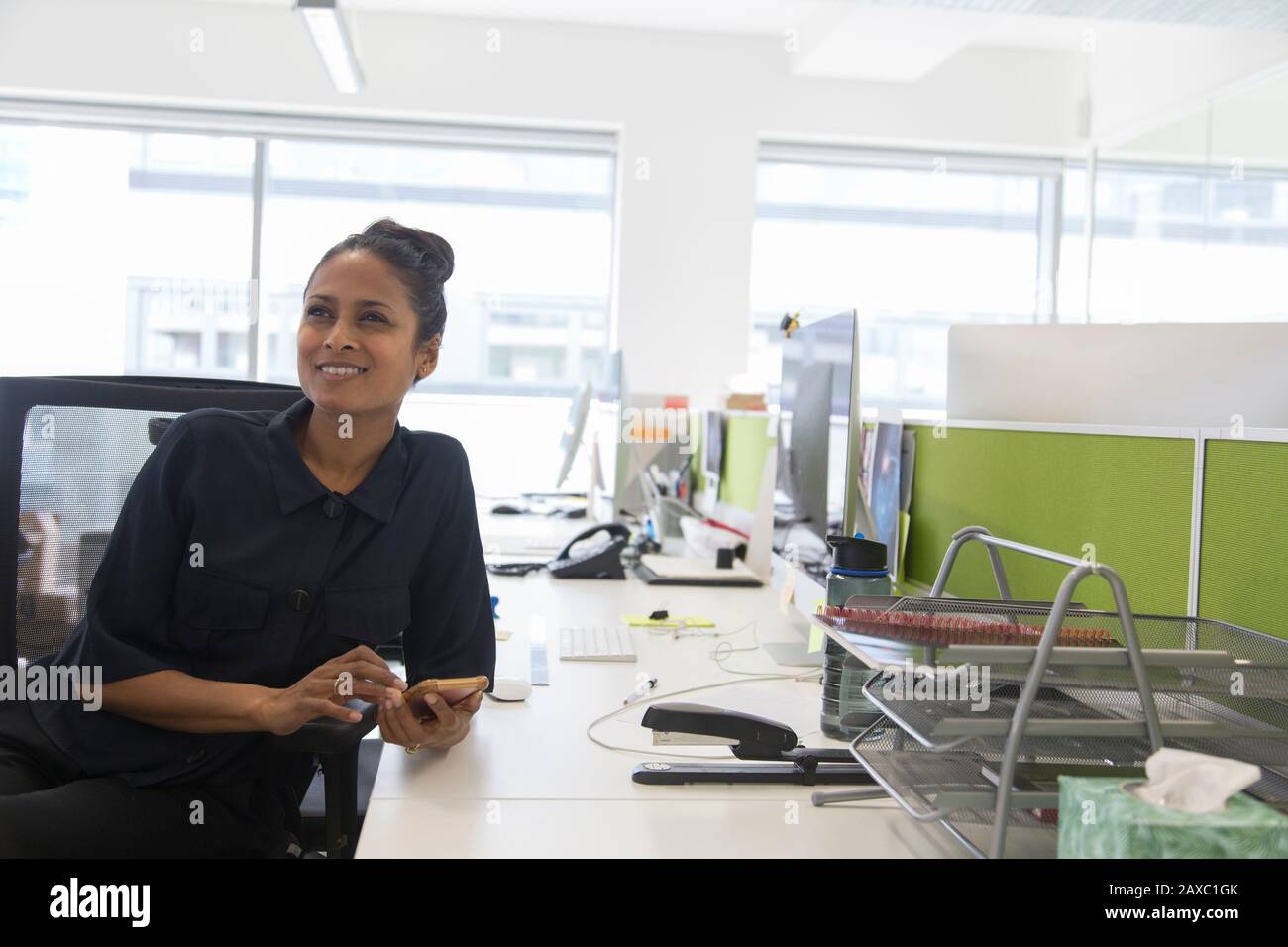 Donna d'affari sorridente che usa lo smartphone nell'ufficio open space Foto Stock