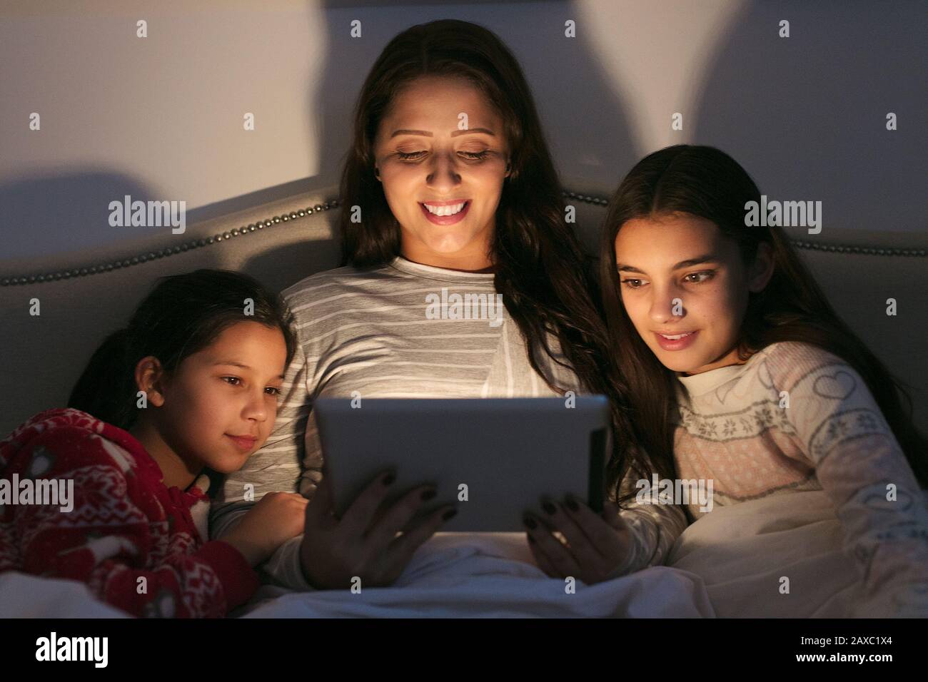 Madre e figlie che usano un tablet digitale in camera oscura Foto Stock
