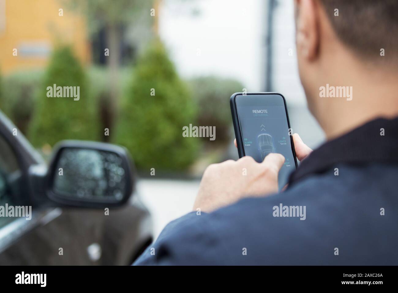 Uomo che imposta l'allarme auto da smartphone in vialetto Foto Stock