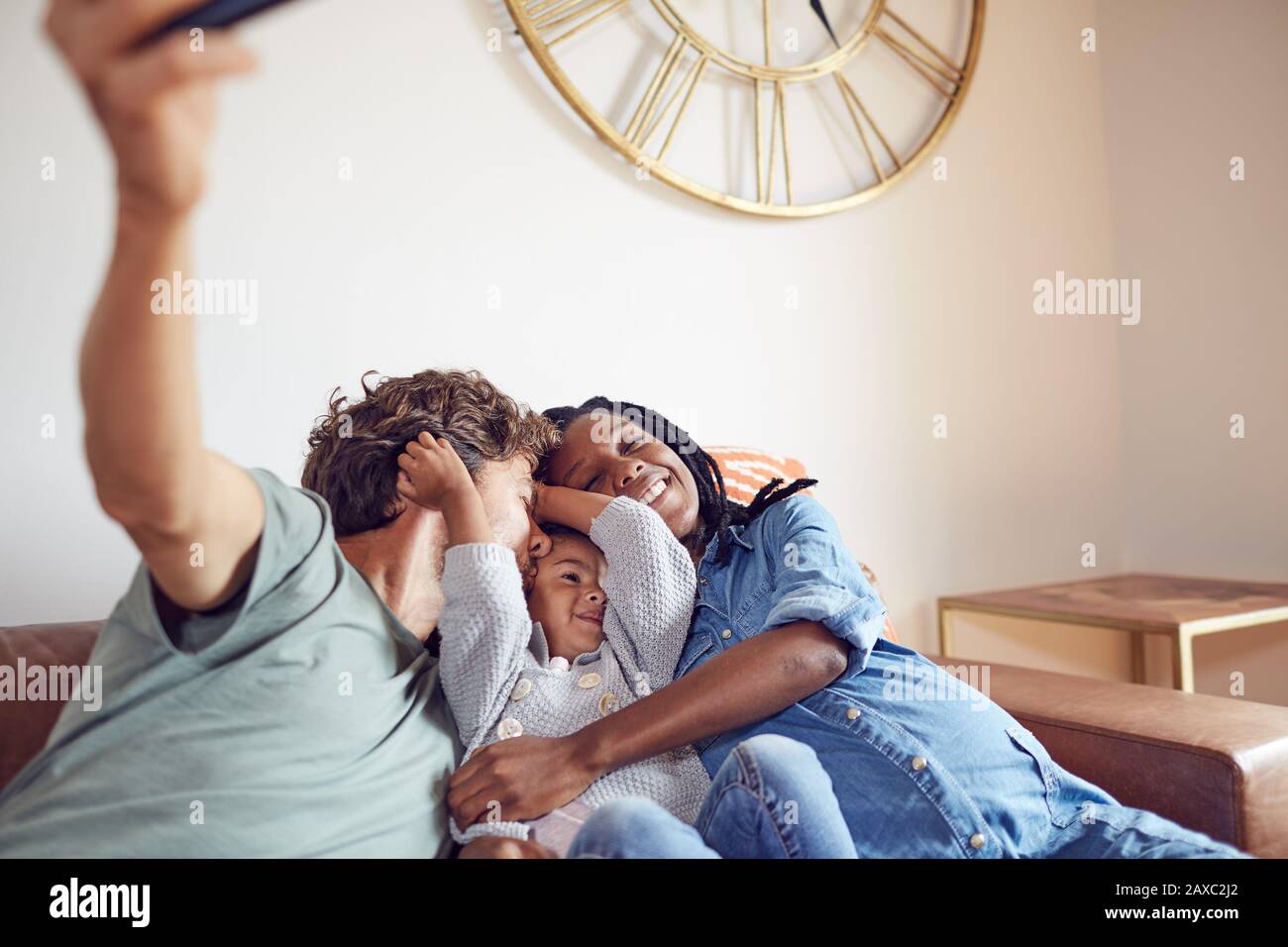 Affettuosa giovane famiglia incinta che prende selfie sul divano del soggiorno Foto Stock