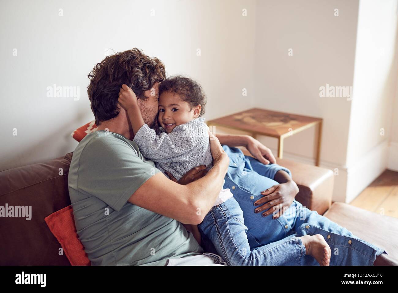 Affettuoso giovane incinta famiglia coccolarsi sul divano Foto Stock