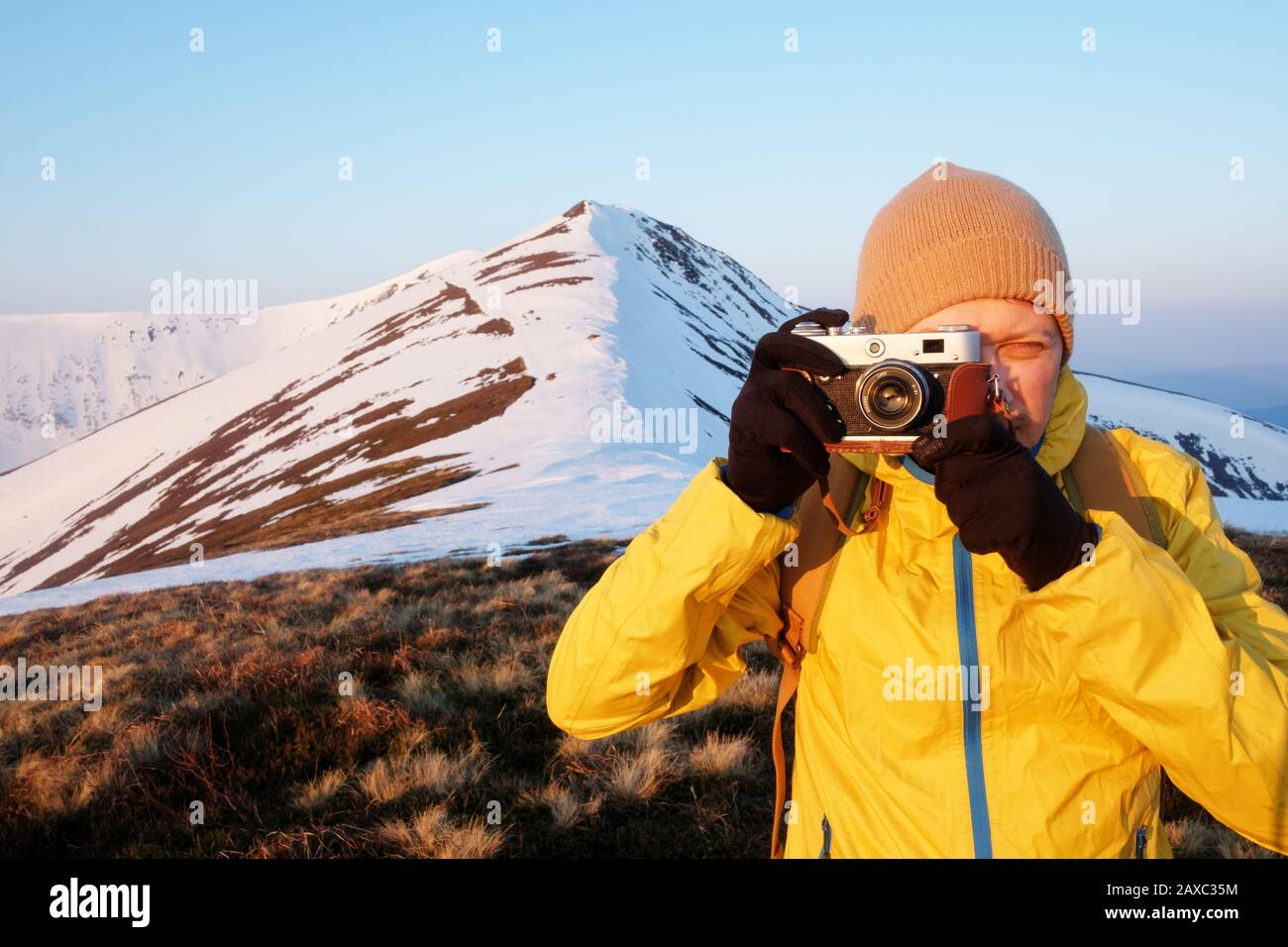 Fotografo in giacca gialla prendendo foto sulla neve campo invernale Foto Stock