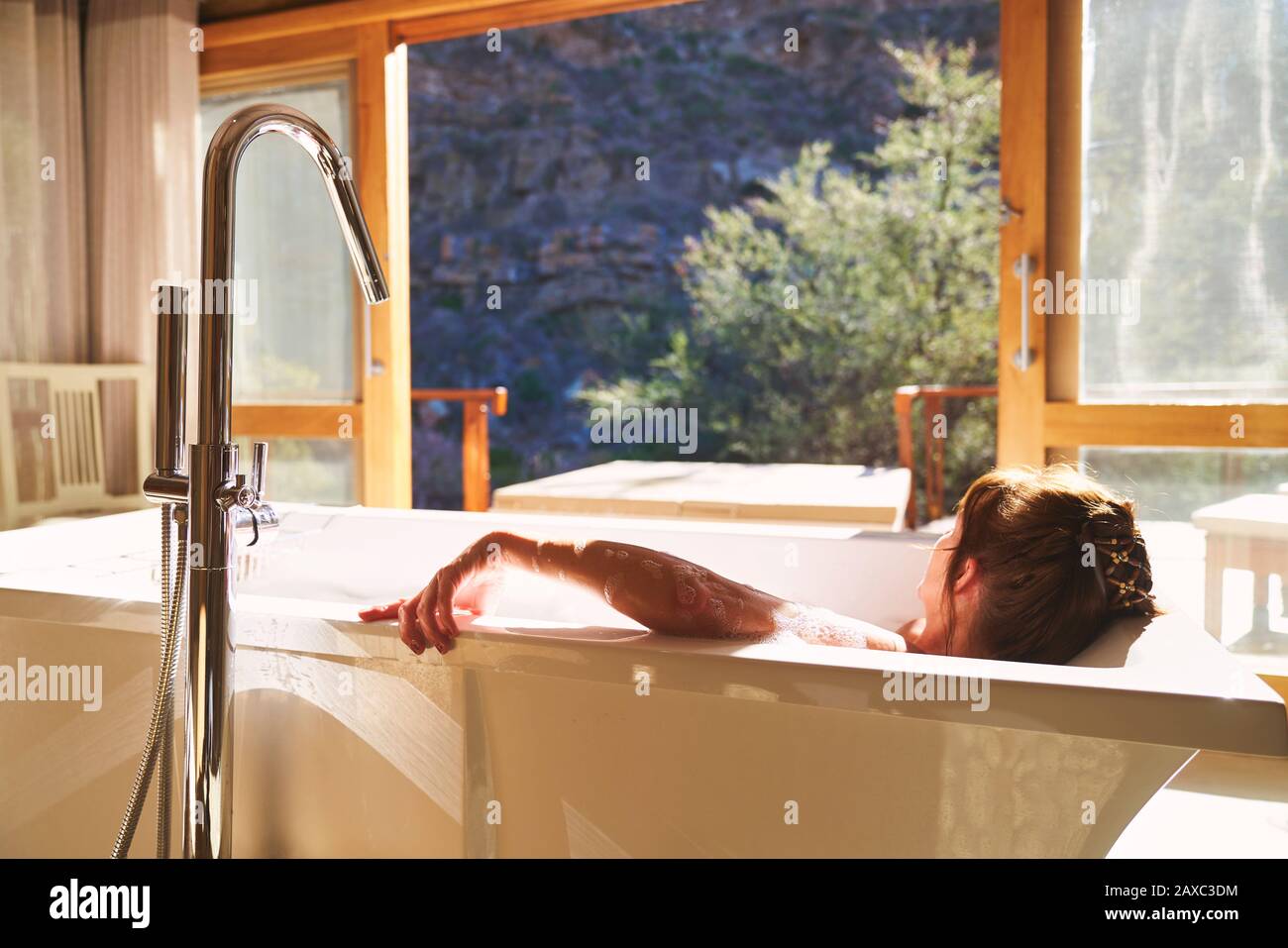 Donna serena che prende un bagno nella soleggiata camera d'albergo Foto Stock