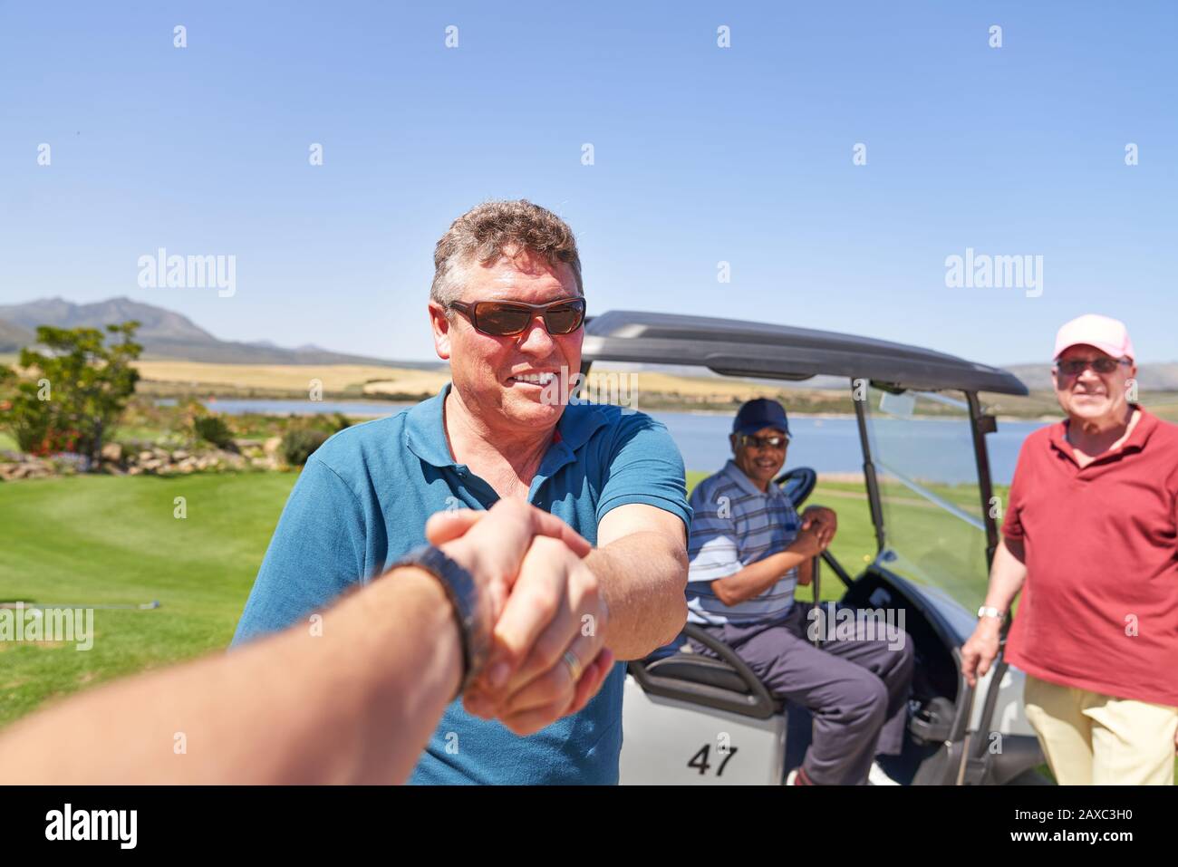 Prospettiva personale golfers maschili handshaking sul campo da golf soleggiato Foto Stock