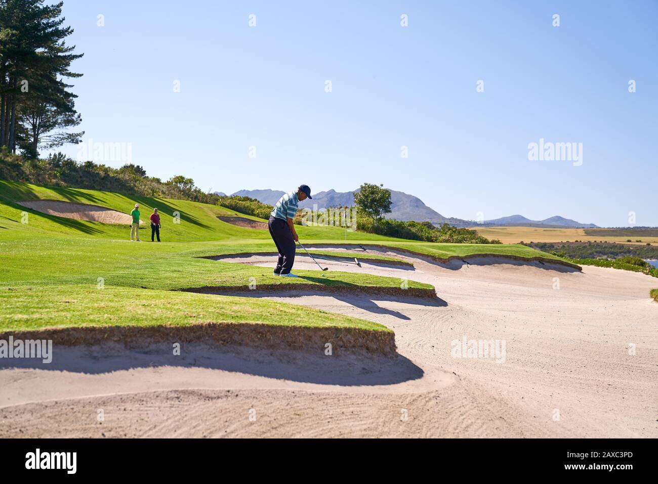 Maschio golfer che prende un colpo sopra la trappola di sabbia soleggiata Foto Stock