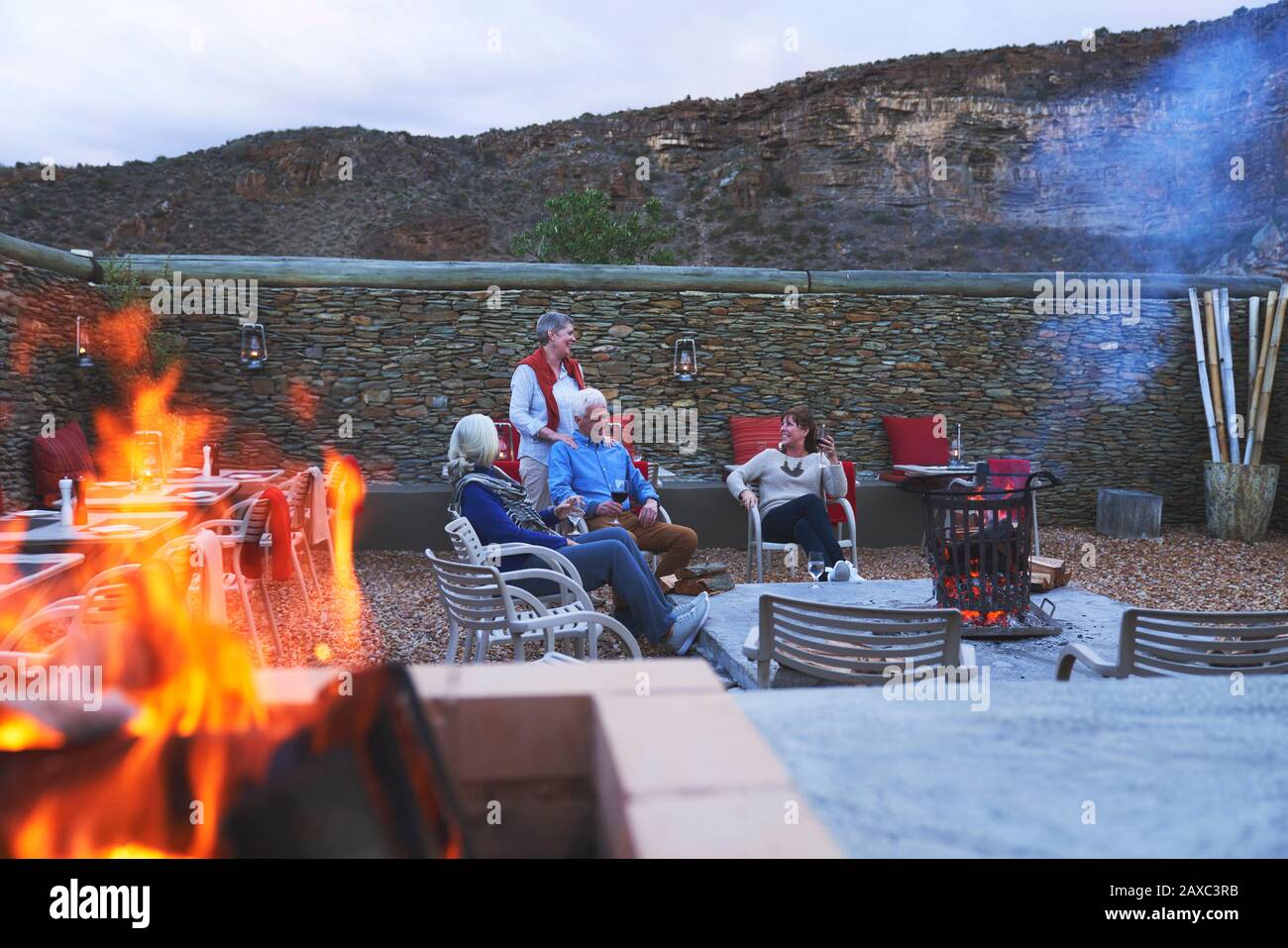 Gli amici senior si rilassano con vino rosso nel patio dell'hotel con caminetto Foto Stock