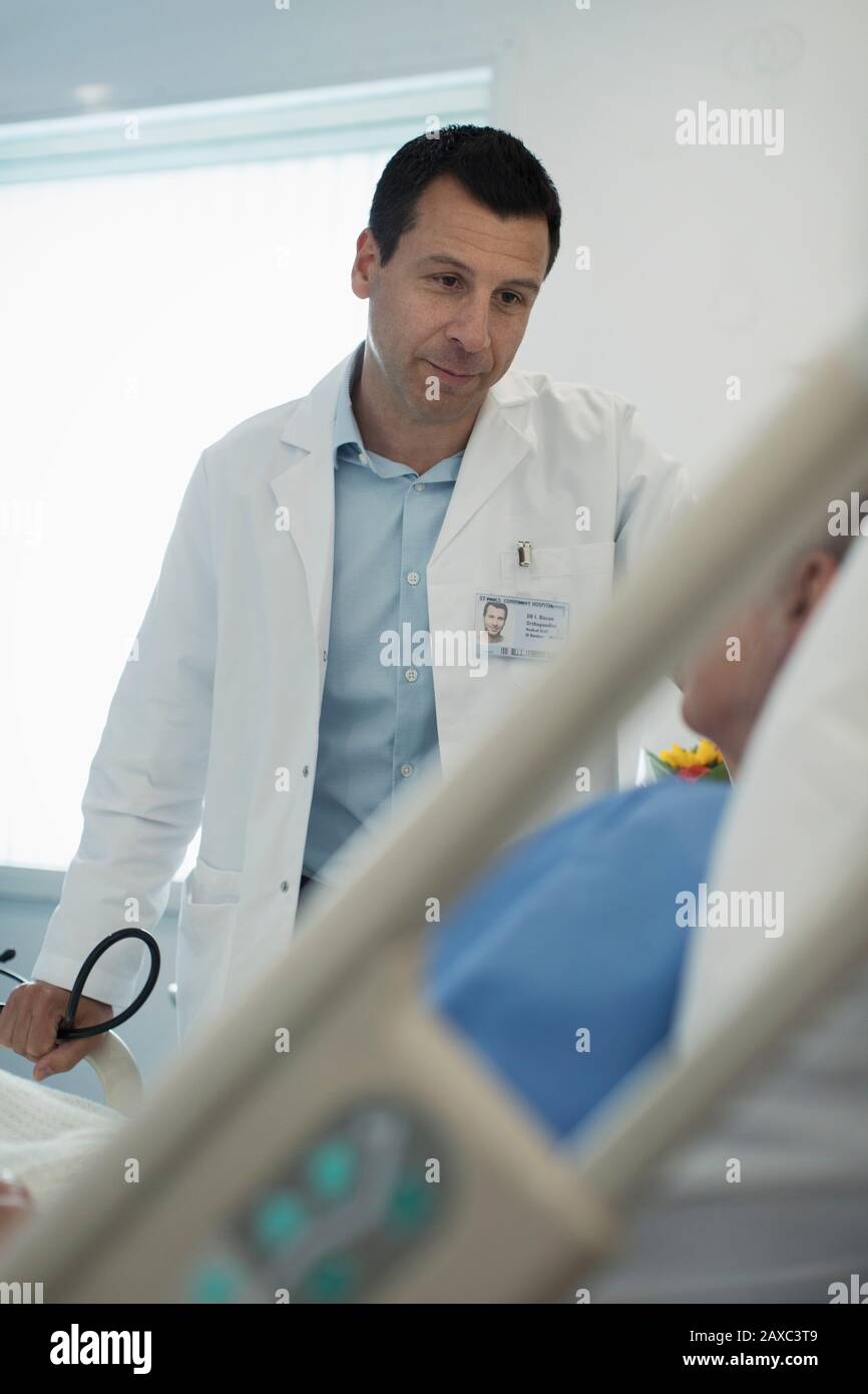 Cura del medico maschile fare giri, parlando con il paziente nella stanza dell'ospedale Foto Stock