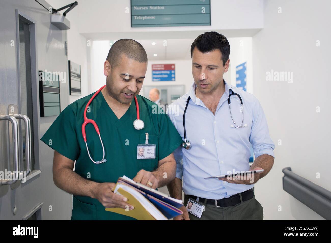 Medico e chirurgo di sesso maschile che discute la cartella medica, facendo giri nel corridoio dell'ospedale Foto Stock
