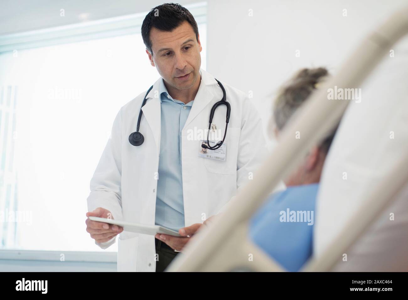 Medico con tablet digitali che si arrotonda, parlando con il paziente nel letto ospedaliero Foto Stock