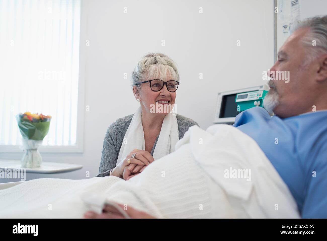 Una donna anziana che si prende cura di visitare, un marito confortante che riposa nel letto dell'ospedale Foto Stock