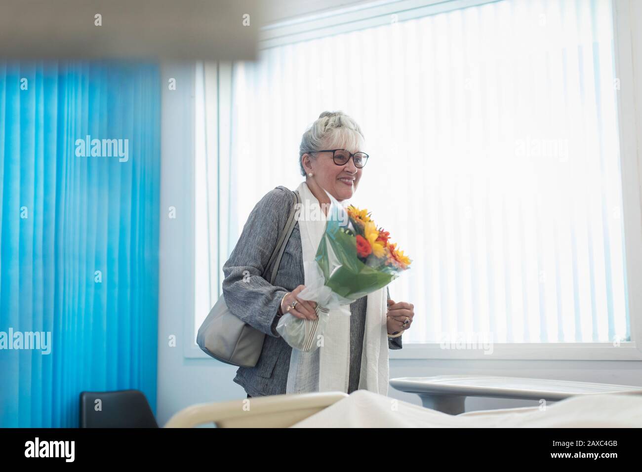 Sorridente ospite femminile con bouquet di fiori in camera d'ospedale Foto Stock