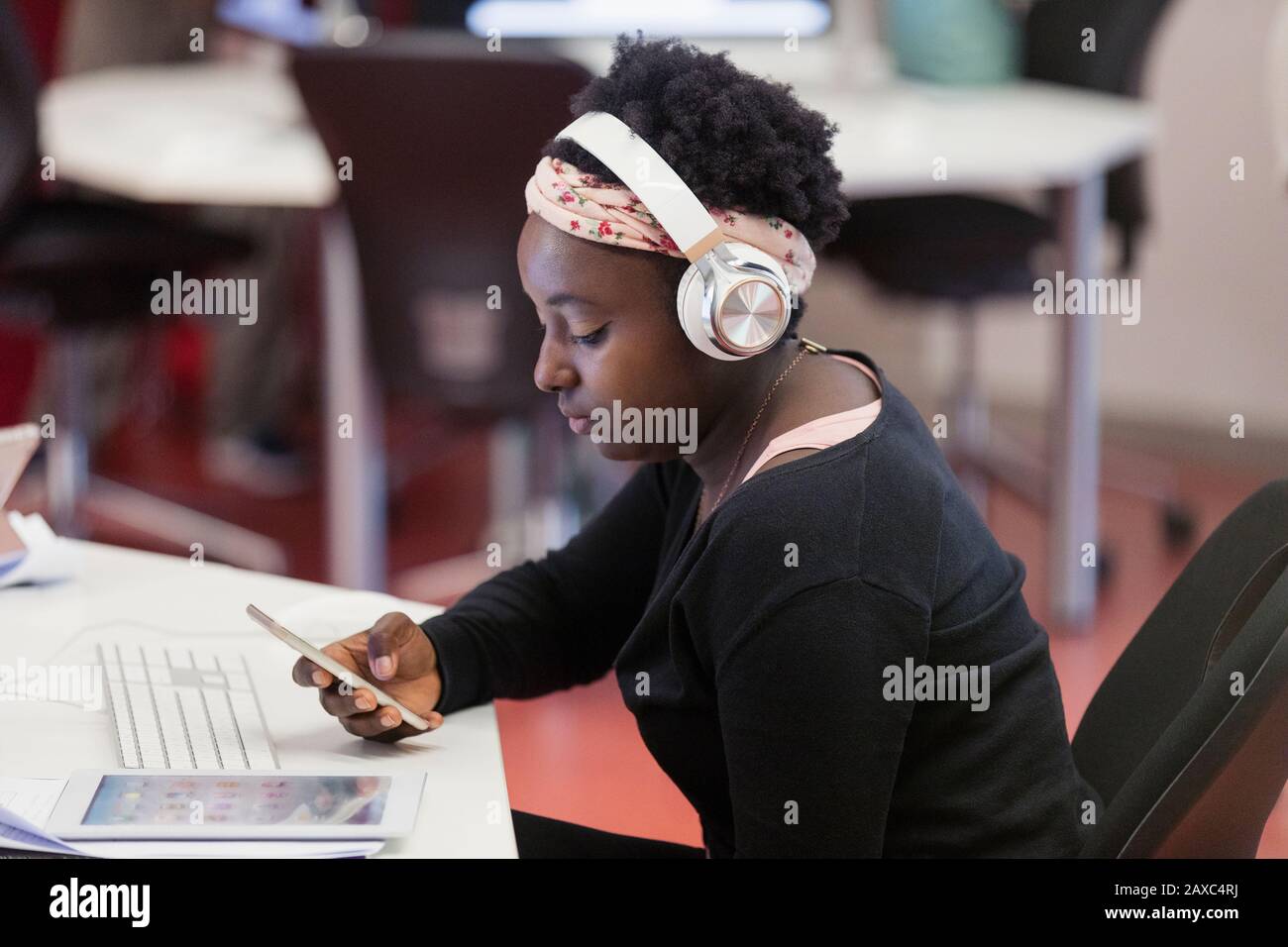 Studente femminile con cuffie che utilizzano lo smartphone in classe Foto Stock