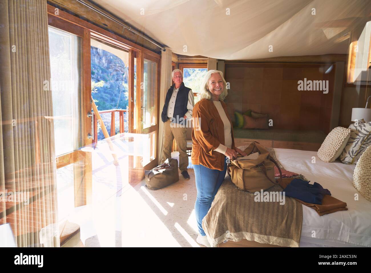 Ritratto felice senior coppia disimballaggio in soleggiata camera d'albergo Foto Stock