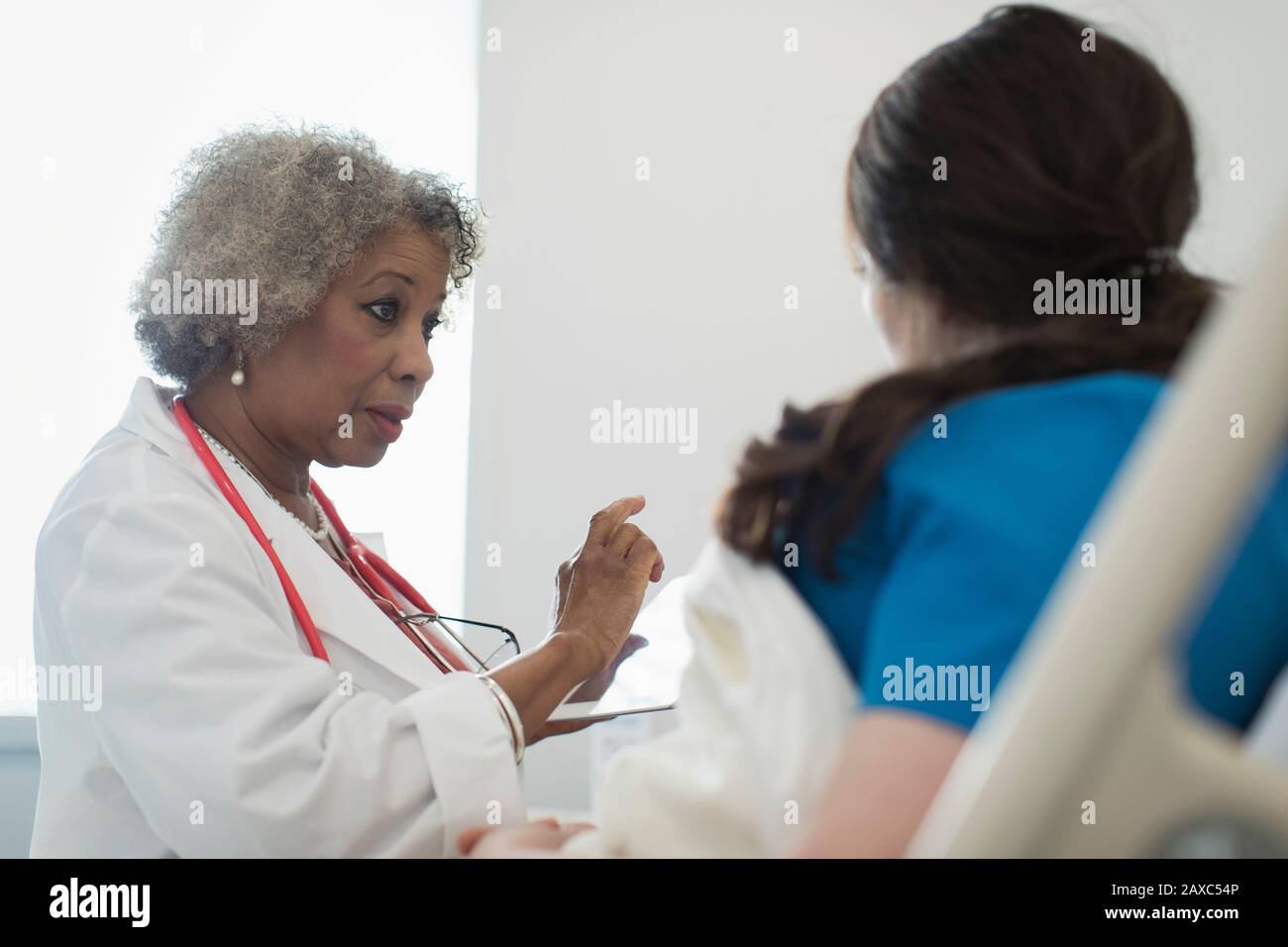 Medico femminile senior con tablet digitali che si arrotonda, parlando con il paziente nel letto ospedaliero Foto Stock