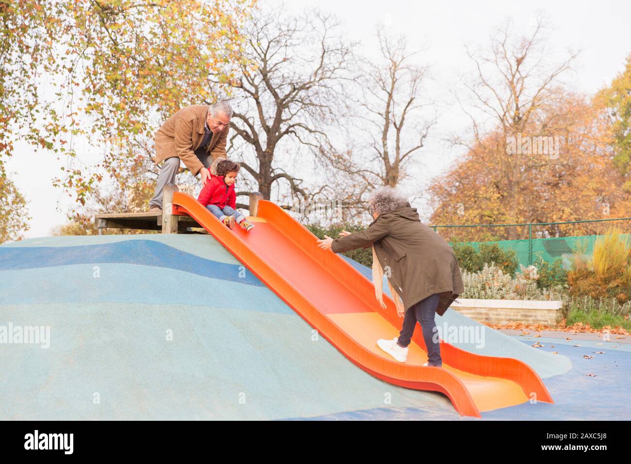 Nonni che giocano con il nipote sullo scivolo del parco giochi Foto Stock