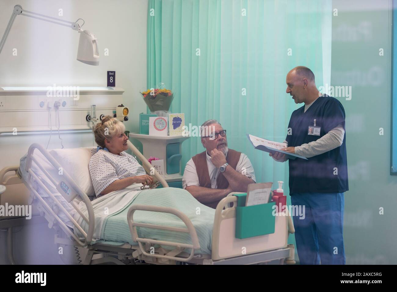 Medico con cartella medica che parla con la coppia senior in stanza dell'ospedale Foto Stock