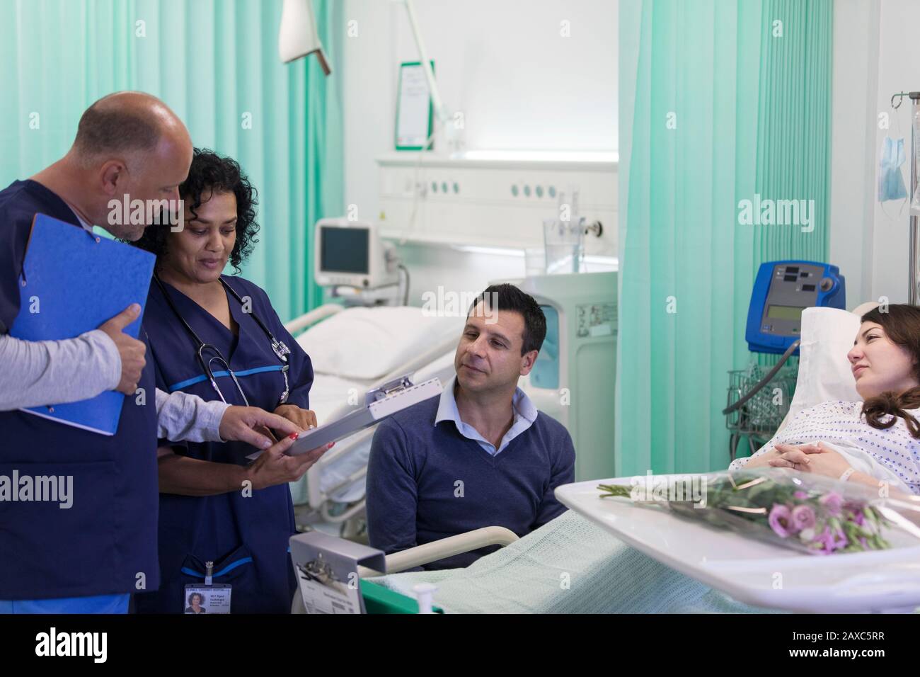 Medici con cartella medica che fa giri, parlando con la coppia nel reparto dell'ospedale Foto Stock