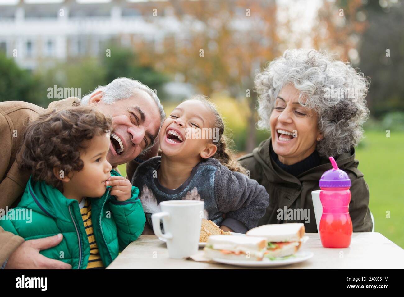 Nonni e nipoti giocosi ridono, mangiando il pranzo nel parco Foto Stock