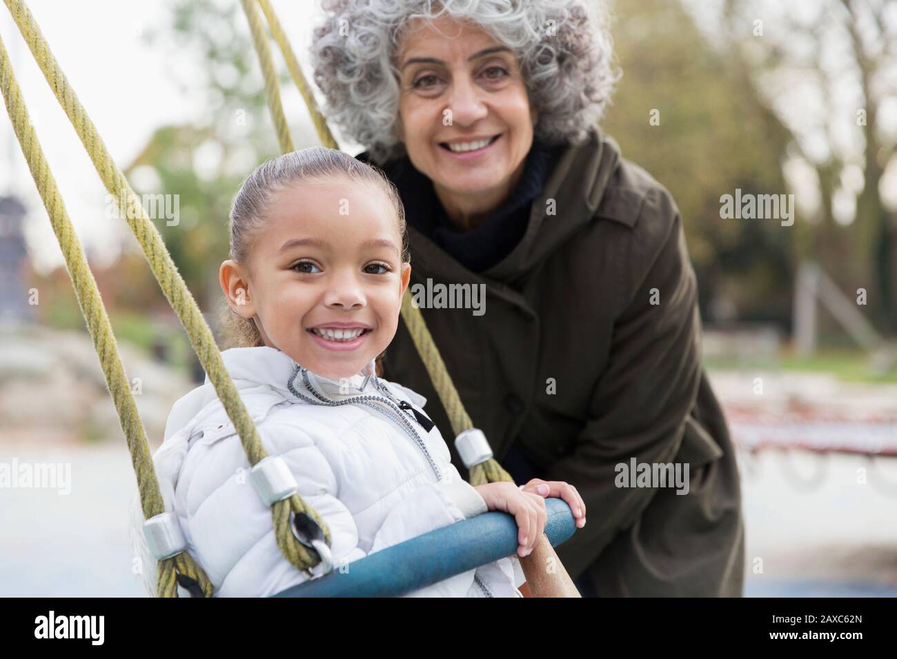Ritratto sorridente nonna e nipote giocando su swing al parco giochi Foto Stock