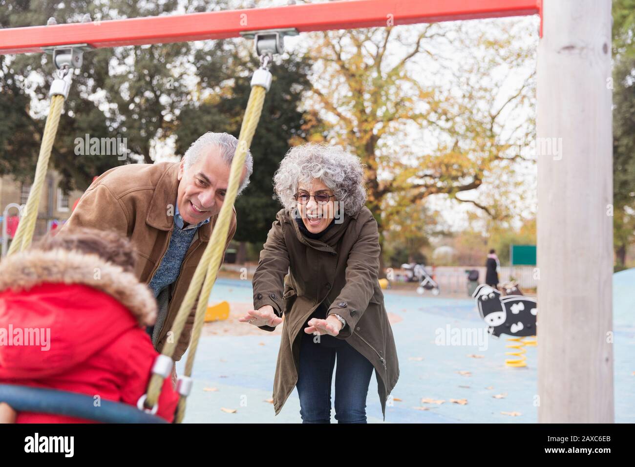 Nonni giocosi che spingono il nipote del bambino nell'altalena al parco giochi Foto Stock