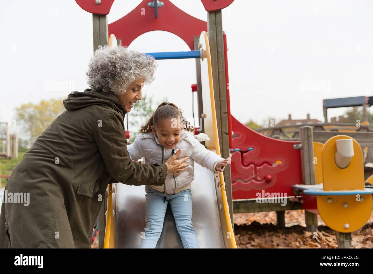 Nonna che gioca con la nipote sullo scivolo del parco giochi Foto Stock