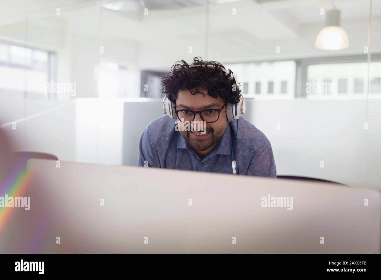Uomo d'affari sorridente con le cuffie che lavorano al computer in ufficio Foto Stock