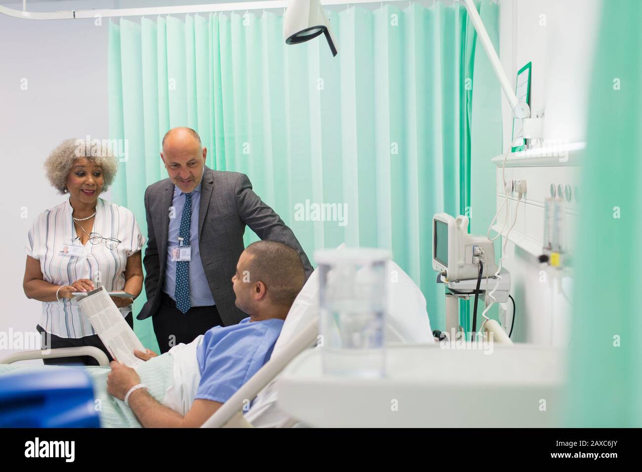 Medici che fanno giri, parlando con il giornale di lettura del paziente nella stanza dell'ospedale Foto Stock