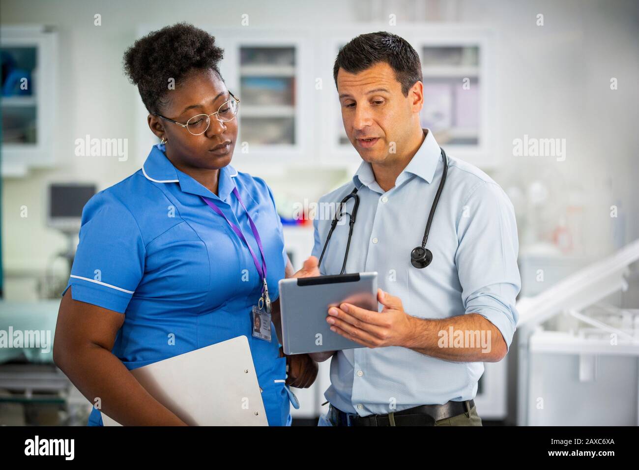 Medico di sesso maschile con compressa digitale che parla con l'infermiere di sesso femminile in ospedale Foto Stock