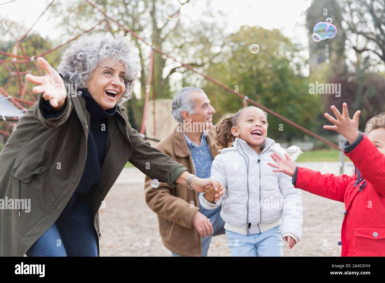 Nonni e nipoti giocosi che giocano con le bolle nel parco Foto Stock