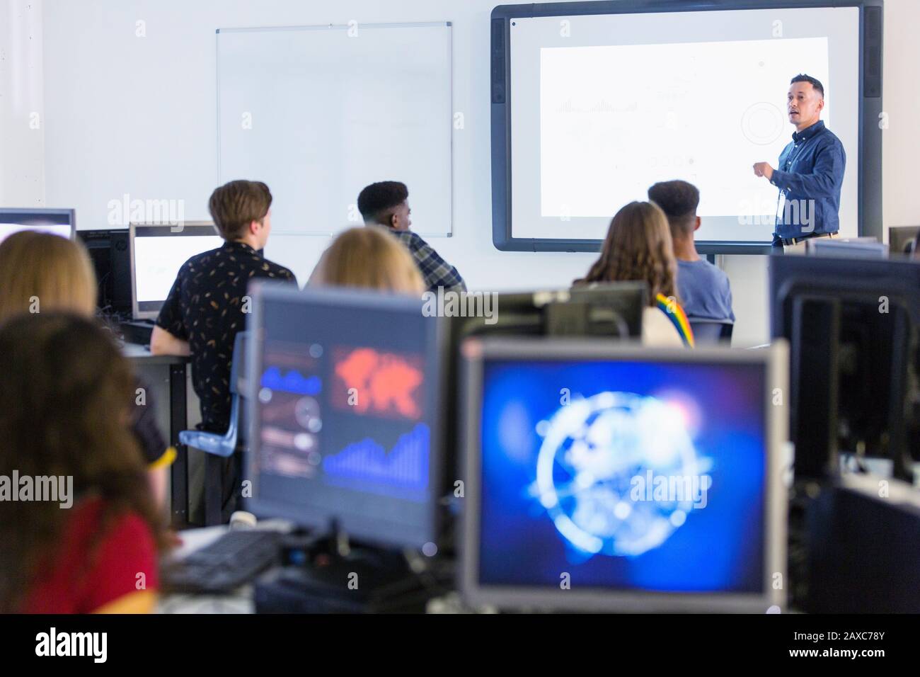 Giovani studenti di alto livello a computer che guardano l'insegnante a schermo di proiezione in classe Foto Stock