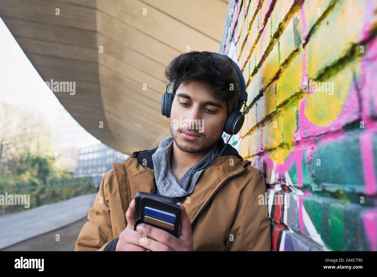Giovane uomo con cuffie che ascolta la musica sul marciapiede urbano Foto Stock