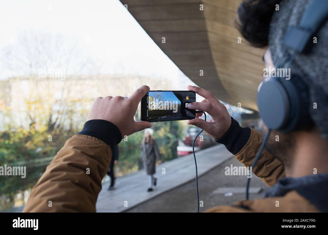 Giovane uomo con le cuffie che usano il telefono della macchina fotografica lungo il canale Foto Stock