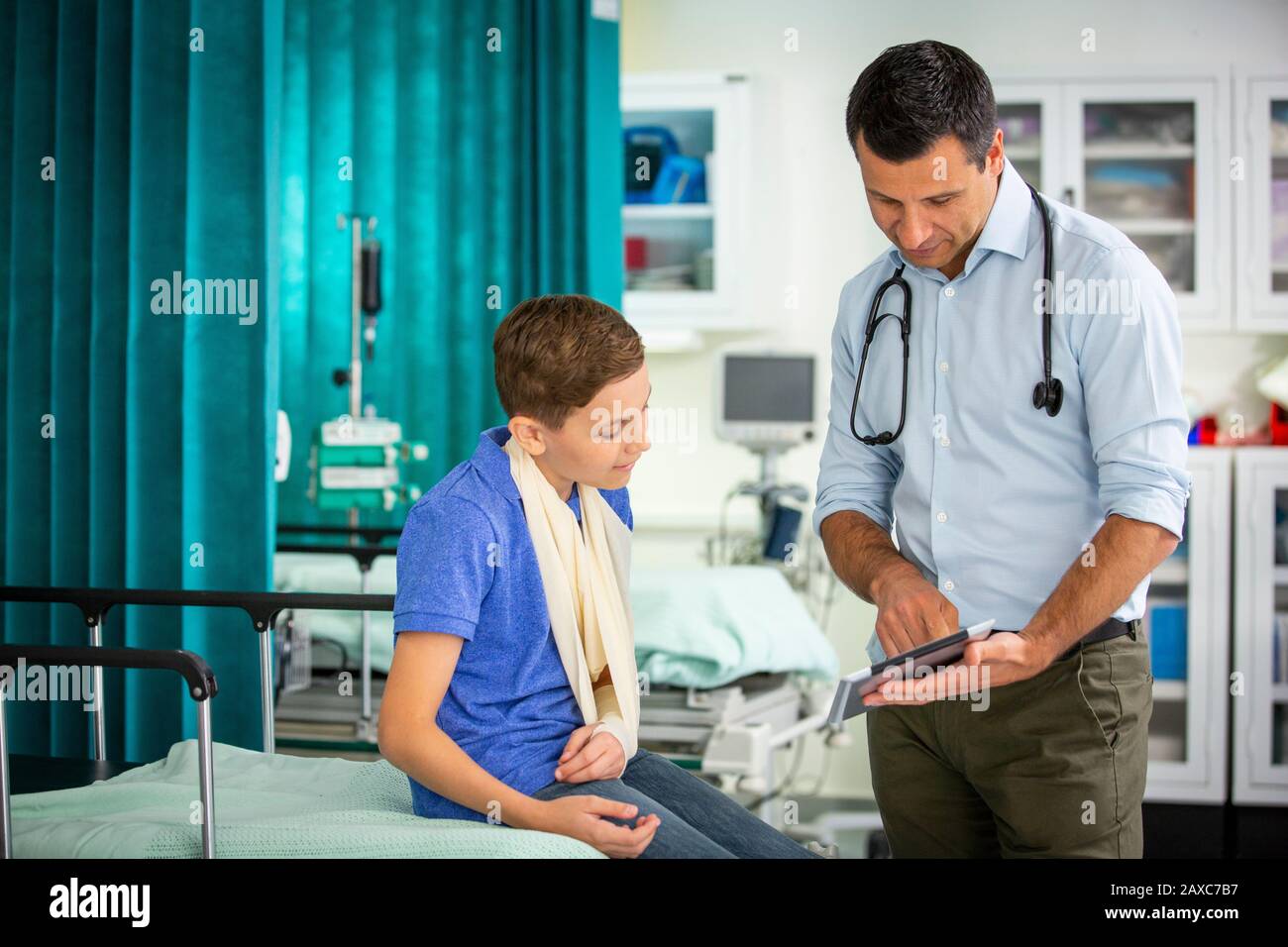 Pediatra maschile che mostra tablet digitale al paziente ragazzo con braccio in imbracatura in ospedale Foto Stock
