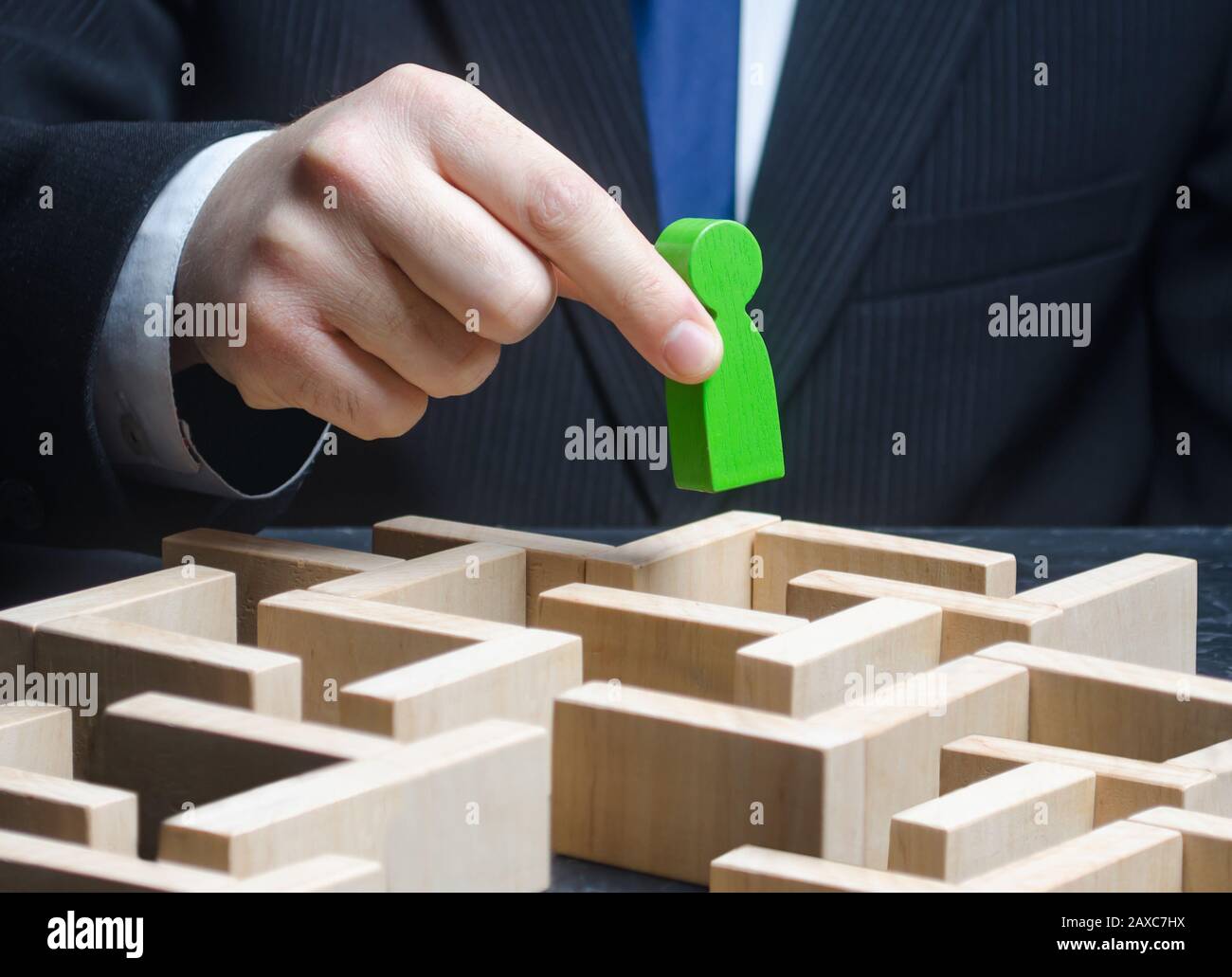 Un uomo d'affari maschio tiene una figura verde sopra un labirinto. Fare un percorso per il successo, fornire supporto. Superato il test, completare l'attività. Competenze professionali sviluppanti Foto Stock