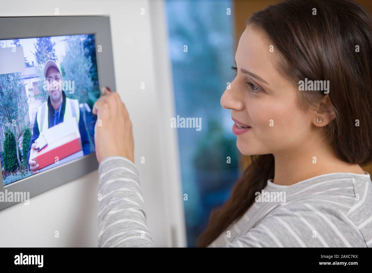 Donna che guarda il deliveryman davanti alla porta dal monitor del sistema di sicurezza domestica Foto Stock