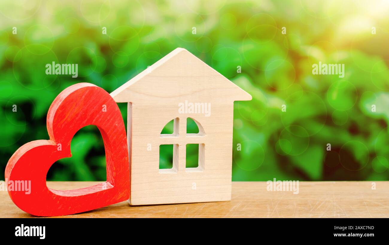 Casa in legno e cuore rosso. Concetto di casa dolce. Assicurazione di proprietà. Una nuova casa per la famiglia. Noleggia una casa il giorno di San Valentino. Comfort per tutta la famiglia. Afforda Foto Stock